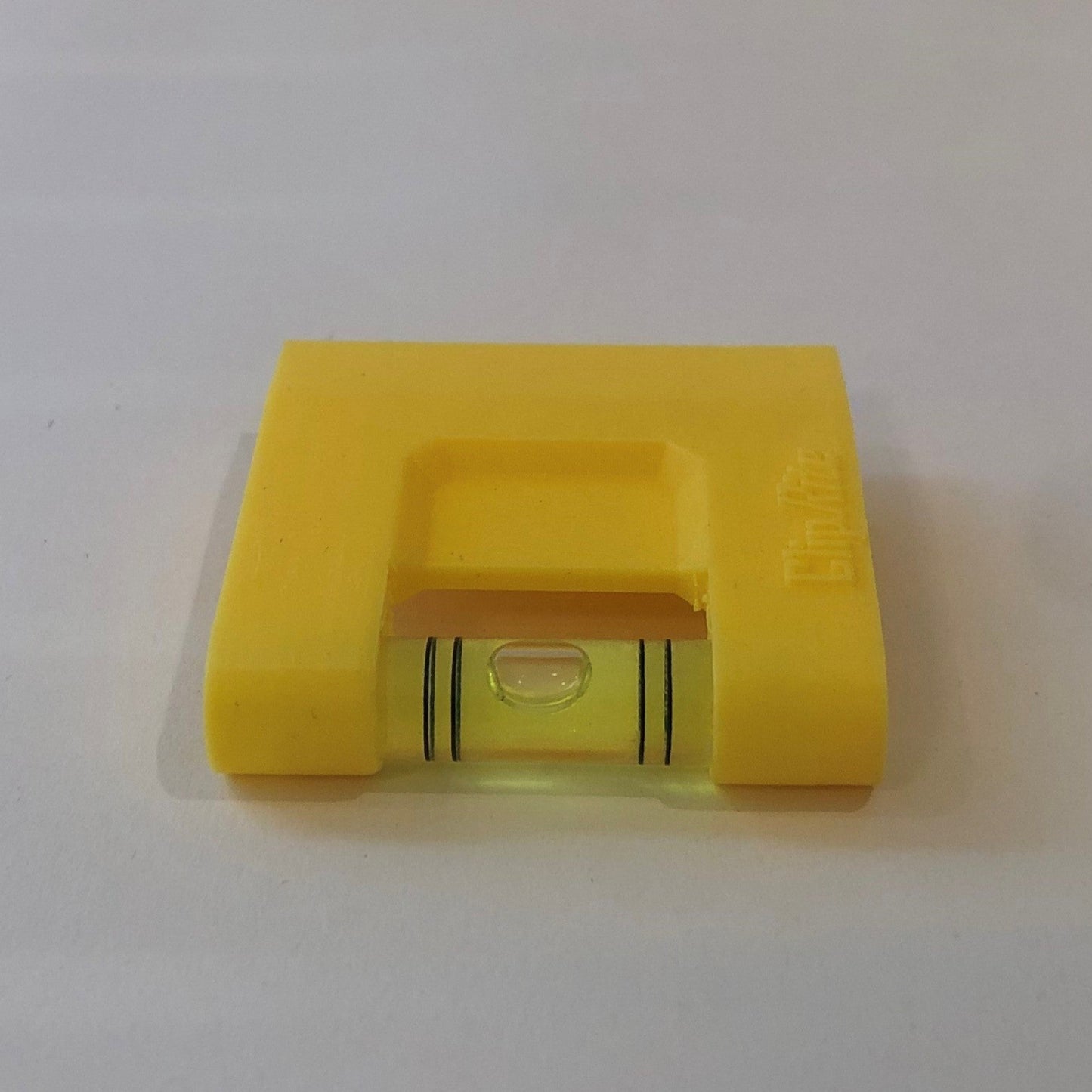 Yellow hands-free plastic clip-on level, designed for easy attachment to surfaces, featuring a built-in bubble vial for precise alignment during leveling tasks for floating picture frames